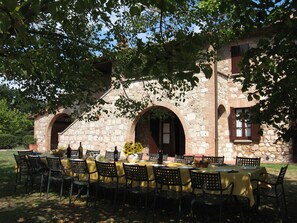Een terras met een stenen gebouw op de achtergrond, met bogen in de deuropeningen en ramen.