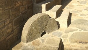 Una escalera de piedra que sube hacia la entrada de un edificio, con un muro de piedra a la izquierda y un área con césped al fondo.