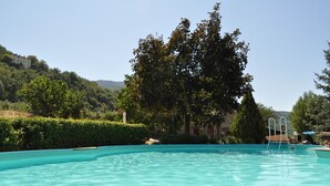 Una piscina con agua cristalina y azul, rodeada de exuberante follaje y un edificio al fondo.