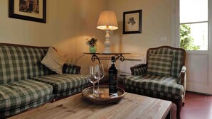 Een gezellige woonkamer met een houten salontafel, twee geruite banken, een lamp en een fles wijn.