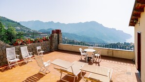 A terrace with outdoor furniture, a stone wall, and a view of mountains.