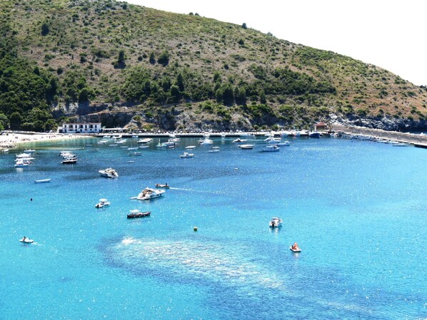 Une zone côtière où des bateaux sont amarrés le long de la rive, avec une plage et une colline en arrière-plan.