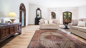 Ein geräumiges Wohnzimmer mit einem großen Holzschrank, zwei beigen Sofas, einem gemusterten Teppich und einem Globus auf einem Stativ.