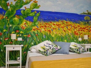 A bedroom with a bed, two bedside tables, and a mural of a cactus field and ocean. - Belice Rooms (Salemi)