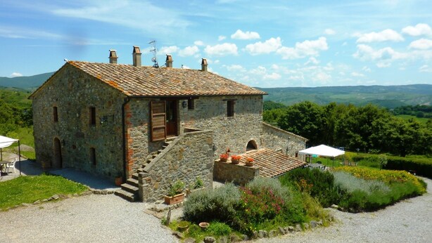 Un bâtiment en pierre avec un toit en tuiles, un escalier menant à un niveau inférieur et un jardin où poussent différentes espèces de plantes.