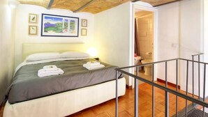 A bedroom with a bed, a nightstand, a framed picture, and a view of a bathroom. - Duplex Apartment (Roma)