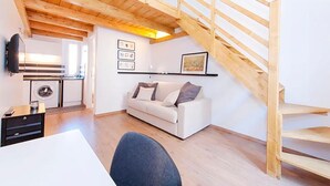 A modern loft apartment with a wooden staircase, a white sofa, a dining table, and a kitchen area. - Duplex Apartment (Roma)