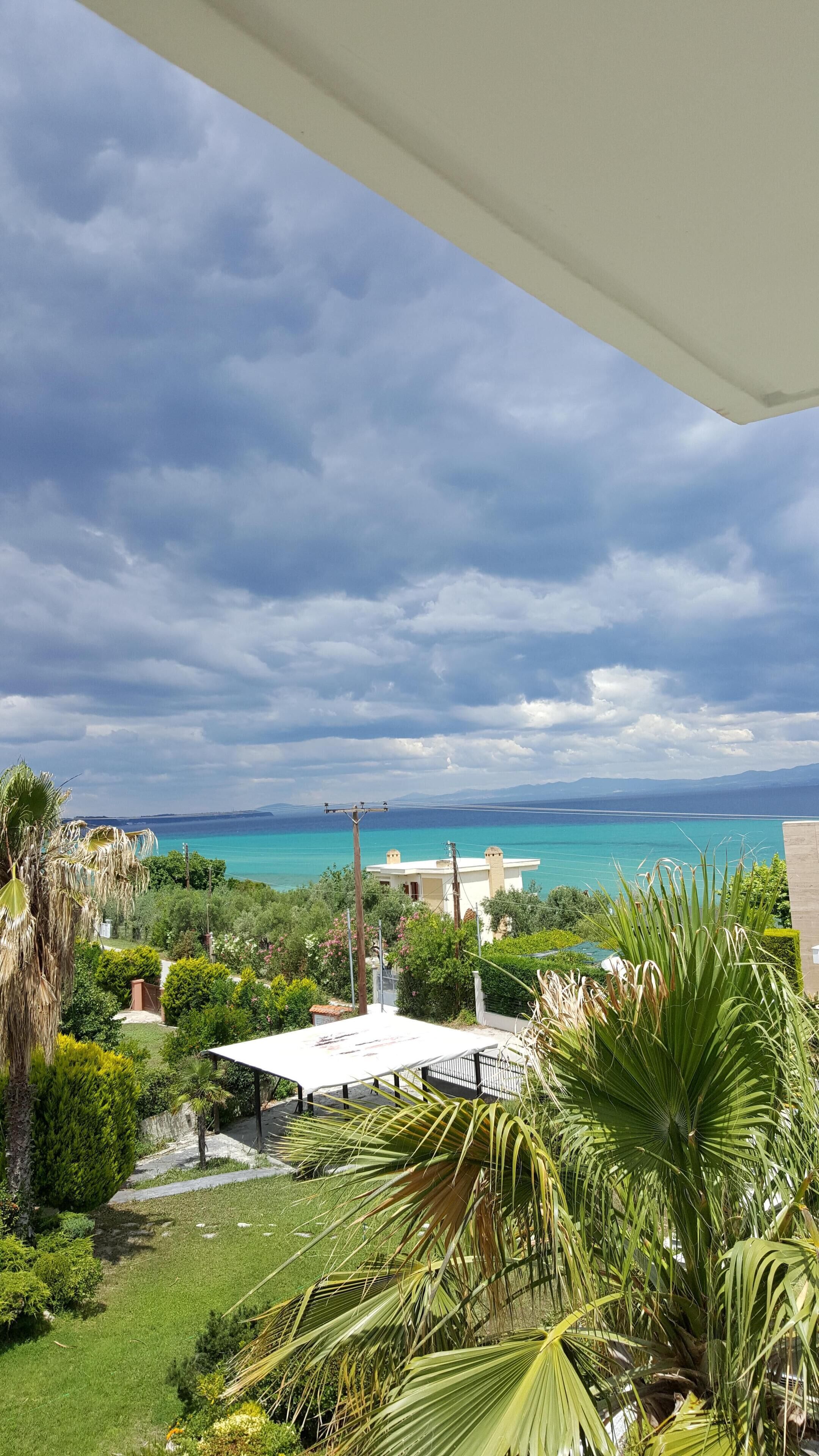 A coastal view with a clear sky, a white building, and lush greenery.