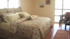 Un dormitorio con cama, una silla, ventilador de techo y dos cuadros en la pared.
