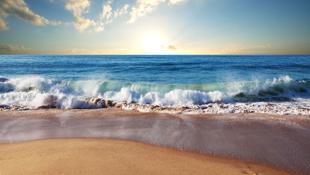 Una playa con olas, cielo despejado y un atardecer.