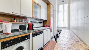 A modern kitchen with white cabinets, a dishwasher, a washing machine, and a countertop with a coffee maker and toaster.