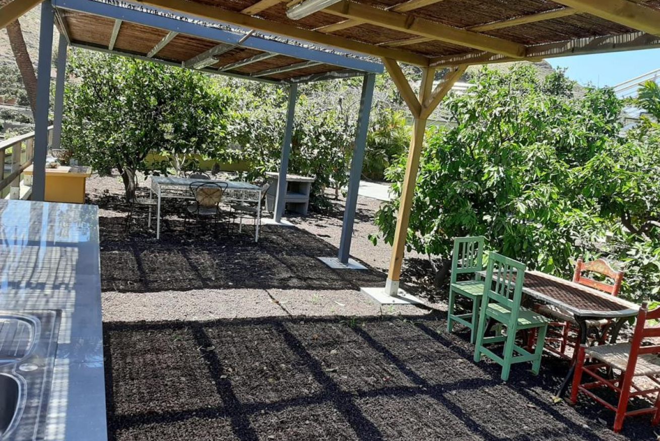 Un espace extérieur aménagé en terrasse, avec une pergola, des tables, des chaises et un jardin.