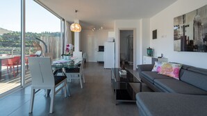 Ein modernes Wohnzimmer mit einer Couch, einem Esstisch und Stühlen. Ein großes Fenster bietet Blick auf Grünflächen und die Stadtlandschaft.