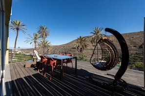 Een terras met een tafel en stoelen, een hangstoel en palmbomen op de achtergrond.
