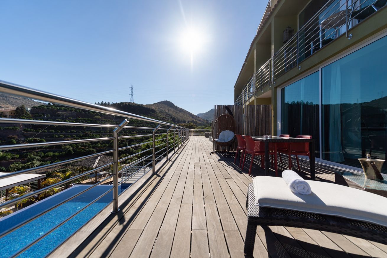 Una terraza soleada con piscina, sillas de descanso y una mesa con sillas.