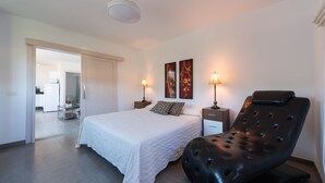 Ein Schlafzimmer mit einem Bett, zwei Nachttischlampen, einem schwarzen Ledersessel und zwei an der Wand befestigten Kunstwerken.