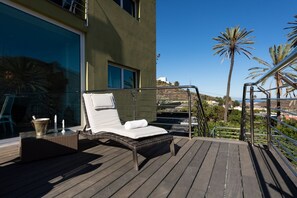Una tumbona en una terraza de madera, con vistas a un edificio y palmeras.