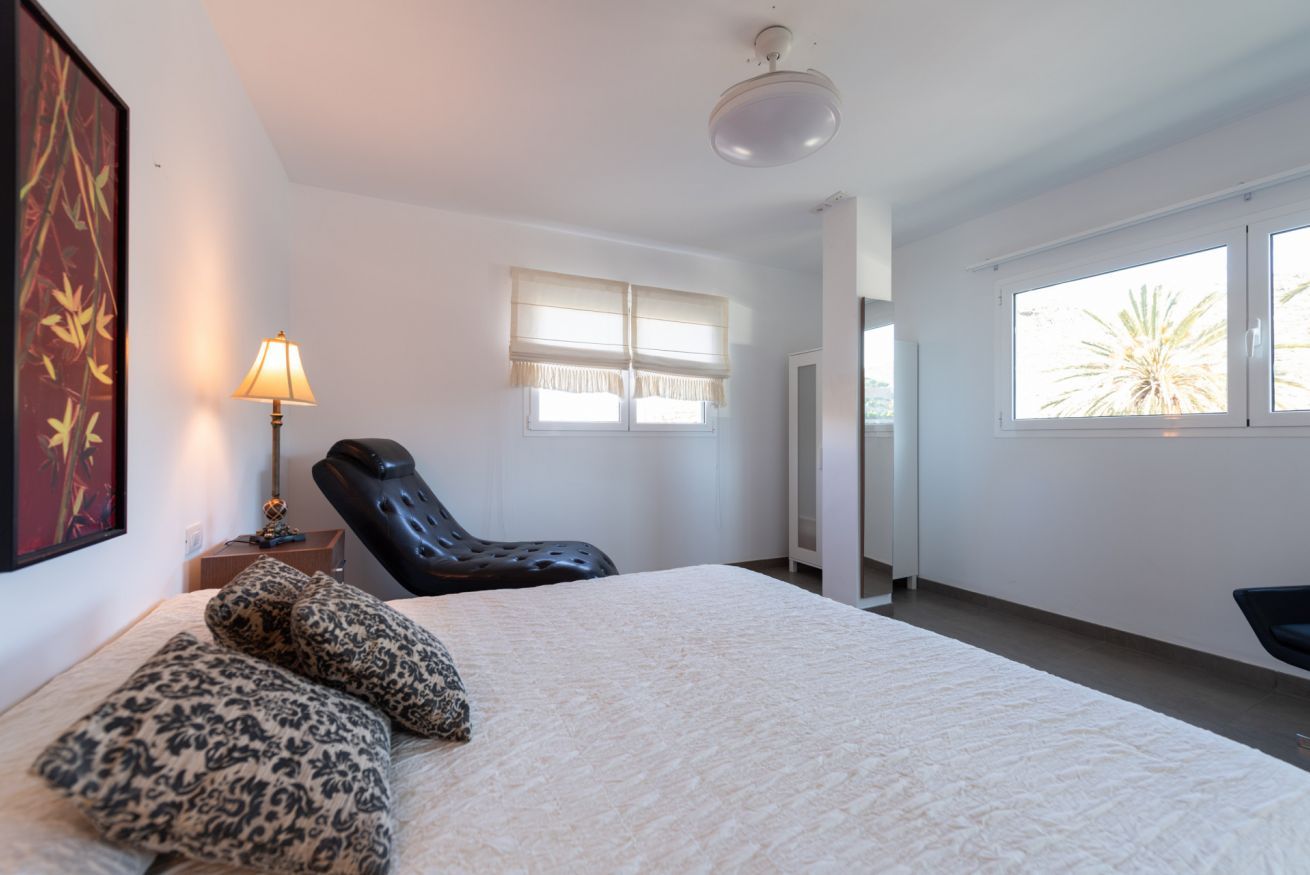 Ein Schlafzimmer mit einem Bett, einem Sessel, einer Lampe und einem Fenster.