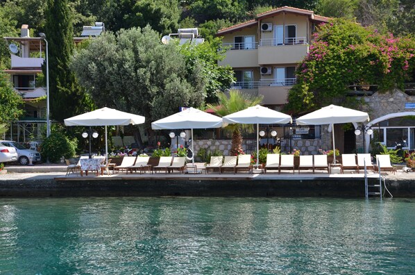 A waterfront hotel with outdoor seating, a pool, and a view of the surrounding buildings and trees.