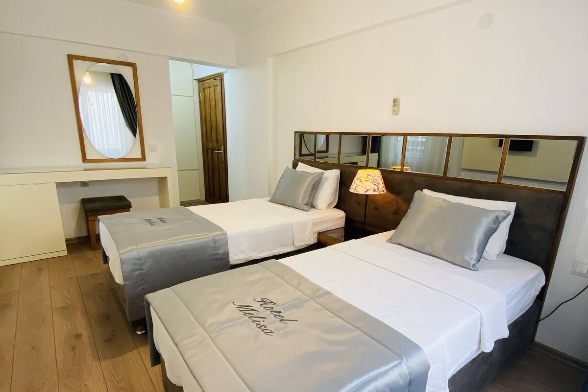 A hotel room with two single beds, a desk, and a mirror.