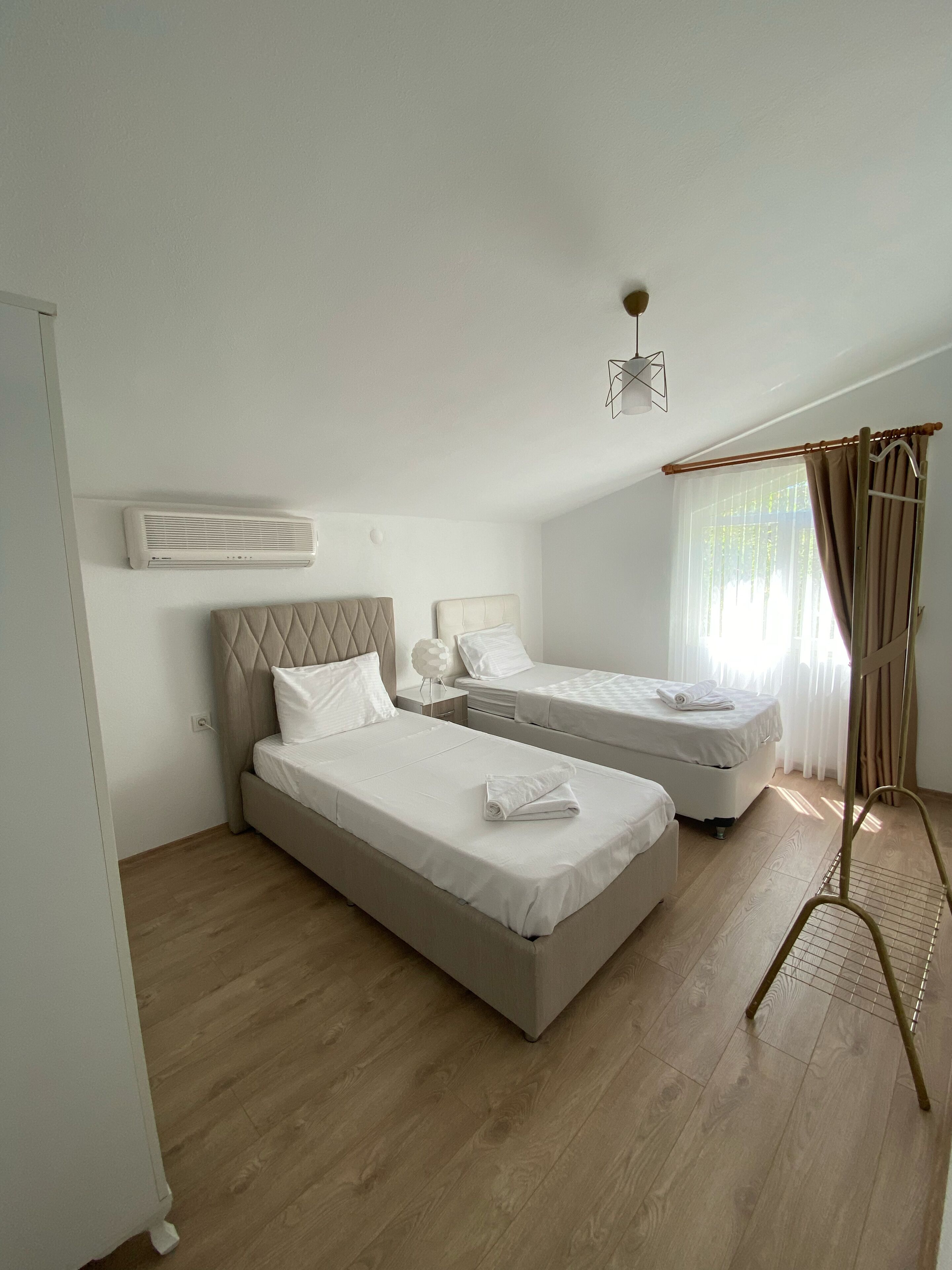 Une chambre avec deux lits, un ventilateur de plafond, une fenêtre avec des rideaux et une lampe sur pied.