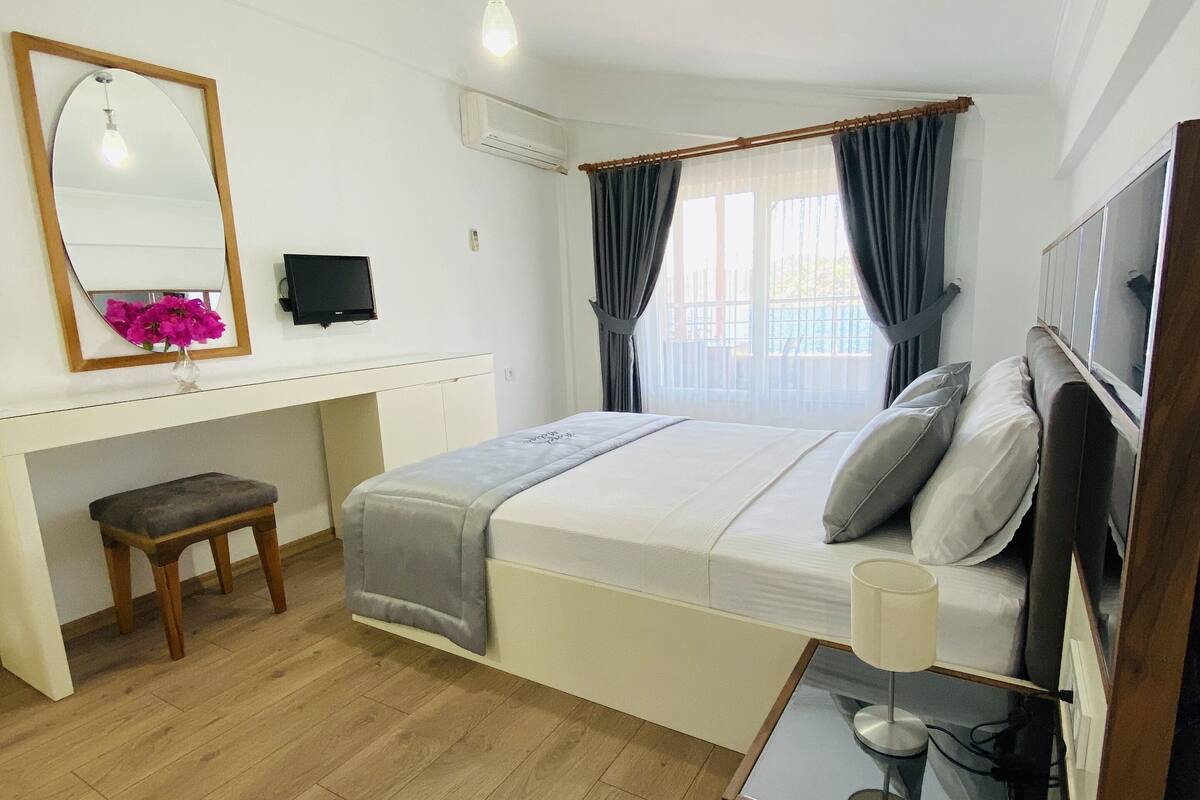 A bedroom with a bed, bedside table, desk, chair, and a mirror.