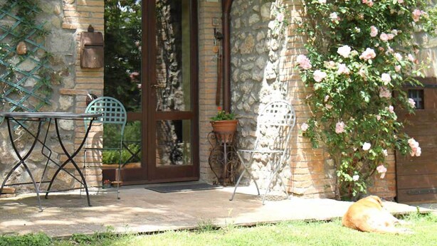 Un bâtiment en pierre avec un porche en bois, une plante en pot et une chaise à l’extérieur.