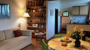 Un salon chaleureux avec un canapé, une petite table sur laquelle est posé un vase de fleurs et une bibliothèque remplie de livres et d’objets décoratifs.