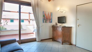 Quarto com porta de vidro deslizante para uma varanda, um armário de madeira, uma TV de tela plana e um quadro na parede.