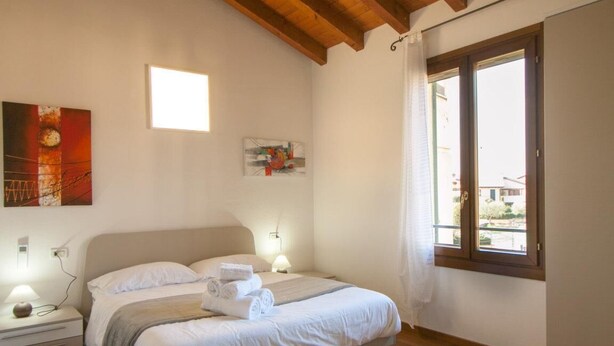 Quarto com cama, mesas de cabeceira, janela e obras de arte nas paredes.