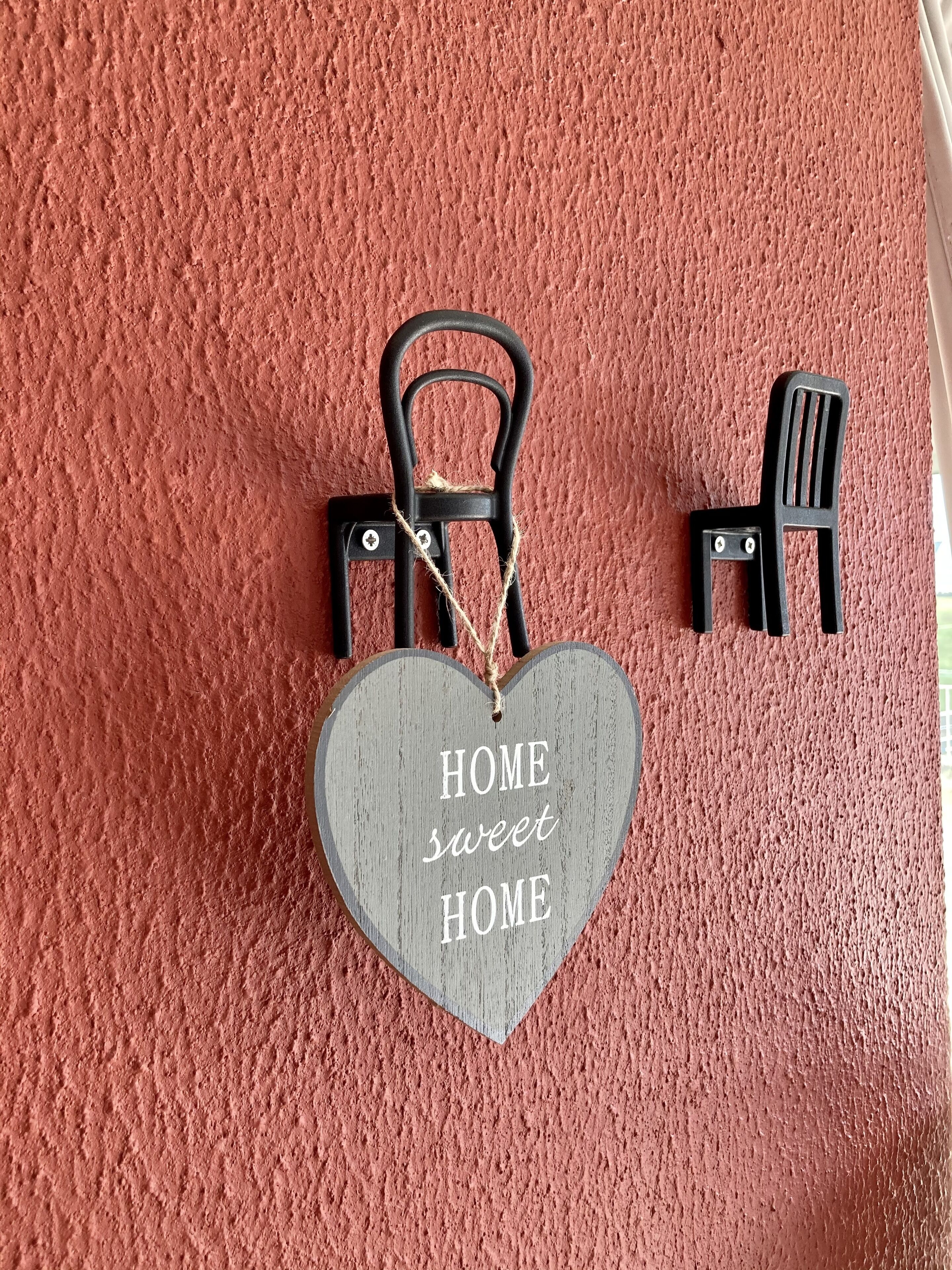 A heart-shaped sign with the text "HOME sweet HOME" hanging on a textured wall.