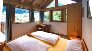 Ein Zimmer mit zwei Betten, einem kleinen Tisch mit Stühlen und einem Fenster mit Vorhängen.