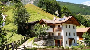 Eine zweistöckige Chalet mit Balkon, umgeben von üppiger Vegetation und einer Bergkulisse.