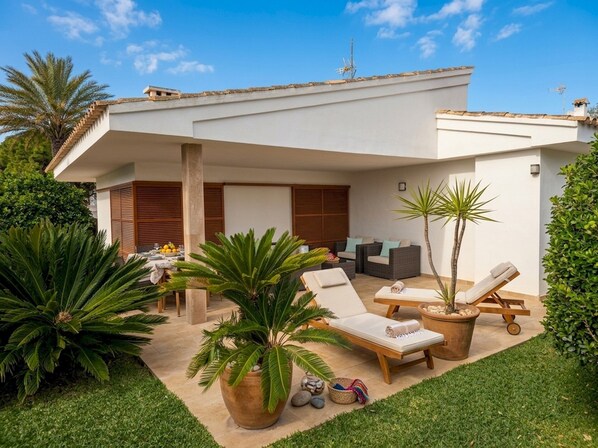 A modern outdoor patio with lounge chairs, a table, and potted plants.