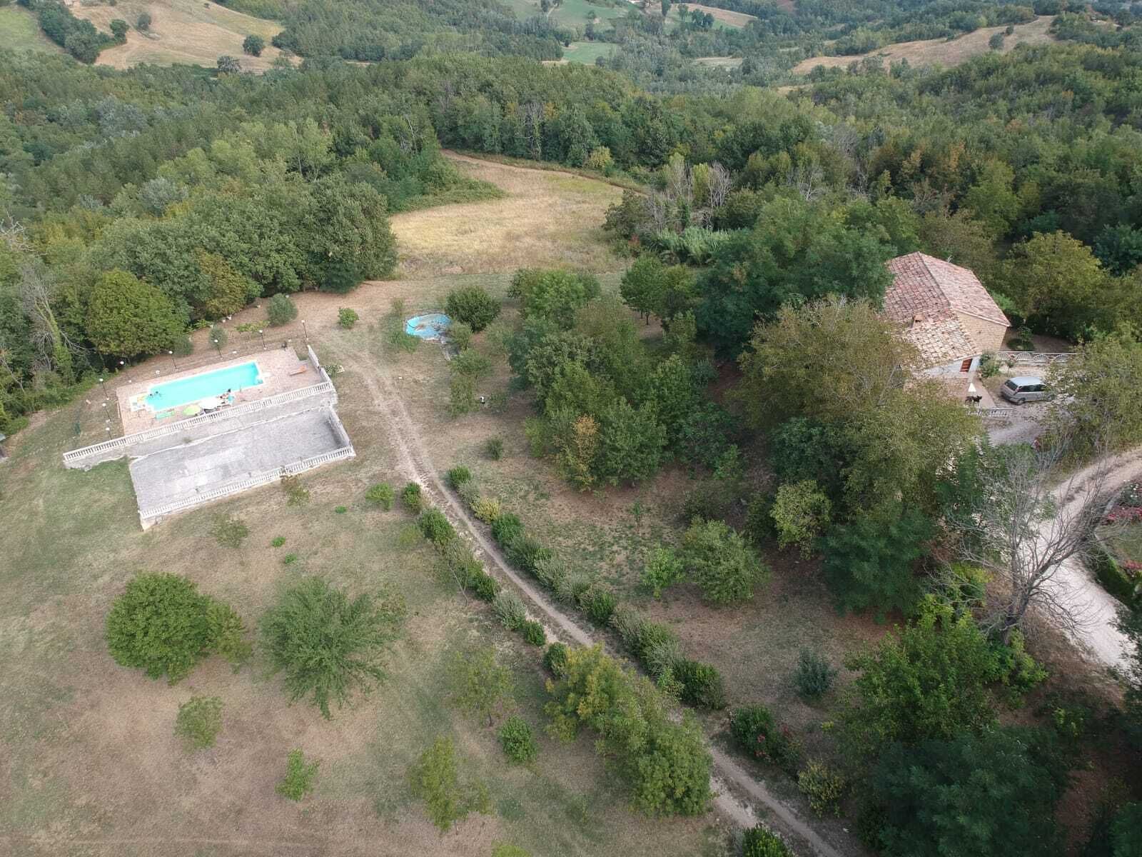 An aerial view of a property with a swimming pool, a small building, and surrounding greenery.
