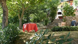 A covered outdoor dining area with a red tablecloth, surrounded by greenery and a stone wall. - Vacation Home Il Rigattiere private pool, nature, absolute relaxation (Gualdo, Macerata)