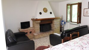 A living room with a fireplace, a television, a sofa, and a dining table. - Vacation Home Il Rigattiere private pool, nature, absolute relaxation (Gualdo, Macerata)