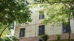 A building with a brick facade and multiple windows, surrounded by trees and foliage. - Vacation Home Il Rigattiere private pool, nature, absolute relaxation (Gualdo, Macerata)
