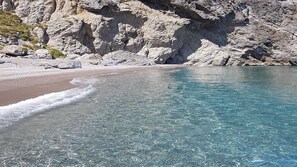 A beach with clear water and rocky cliffs.