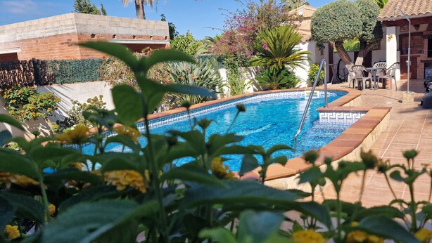 Ein Swimmingpool, umgeben von einer Terrassenanlage mit Gartenmöbeln und einer Backsteinmauer.