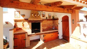 Eine Außenküche mit Backofen aus Ziegeln, Holzbalken und Fliesenboden.