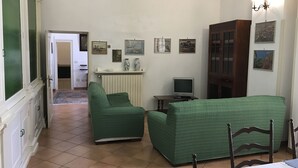 A living room with a green sofa, a television, and a cabinet. There are pictures on the wall and a door leading to another room. - Casa PORTATERRA, Antica Dimora for a peaceful stay in the heart of Salento (Scorrano)