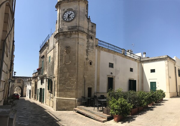 A historic building with a clock tower, a paved courtyard, and outdoor seating.