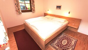 Une chambre avec un lit en bois, une fenêtre ornée de rideaux à motifs floraux, une table de chevet et un tapis.