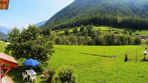 Un paysage rural avec un bâtiment en bois, une table entourée de chaises et un parasol bleu.