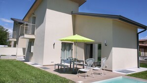 Ein modernes Haus mit Terrasse, Pool und Tisch mit Stühlen.