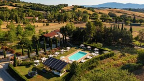 Zona de piscina con sillones de descanso y una fuente de agua con energía solar, rodeada de jardines cuidados y vistas a colinas ondulantes.