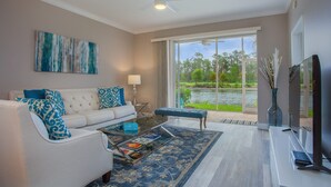 A modern living room with a white sofa, blue patterned pillows, a glass coffee table, and a view of a lake through large windows. - Beautiful 1st. floor unit totally renovated with lake view! (Naples)