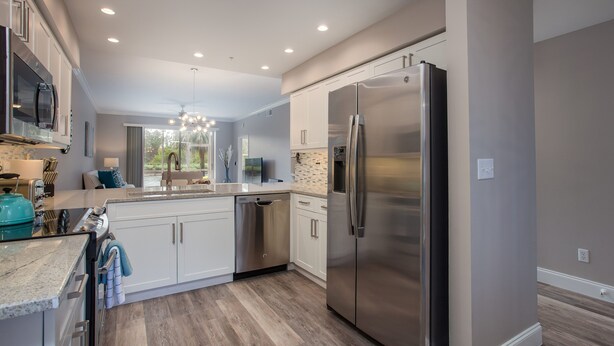 A modern kitchen with white cabinets, stainless steel appliances, and a wooden floor. - Beautiful 1st. floor unit totally renovated with lake view! (Naples)