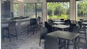 An outdoor dining area with a bar, wicker furniture, and large windows offering a view of the outdoors. - Beautiful 1st. floor unit totally renovated with lake view! (Naples)